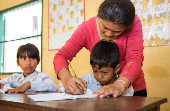 A teacher helps a child write at Krousar Thmey